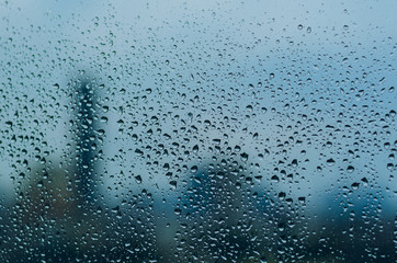 Wall Mural - Rain drop on glass window in monsoon season with blurred city background for abstract and background concept.