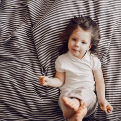 Portrait of beautiful cute little 3 years girl lying on bed in dress and looking at the camera