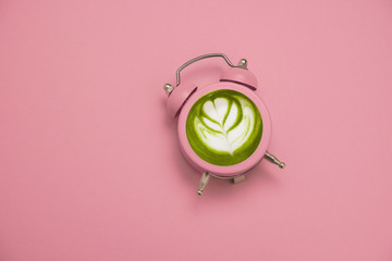 green japanese matcha tea in a pink alarm clock on a pastel pink background copy space, detox and healthy lifestyle time concept