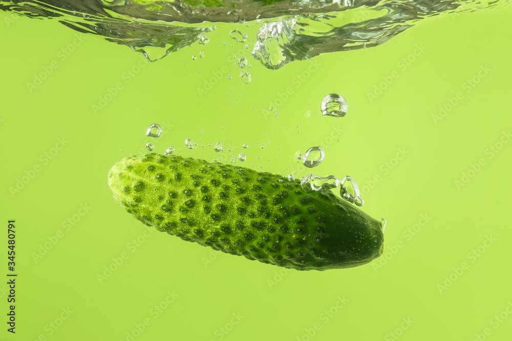 Falling of fresh cucumber into water against color background