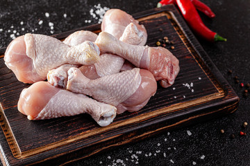 Wall Mural - Raw meat. Chicken legs lie on a wooden board with vegetables and spices on a black background. background image, copy space text