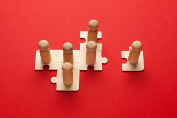 Wooden figures on puzzles on red background as a symbol of team building. Organization group people in business. Cooperation and partnership.