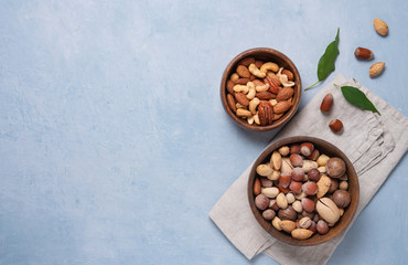 a mixture of nuts in two wooden bowls on gray napkin on a blue background. Vegan product.