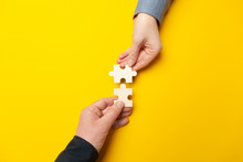 Two Hands Connect Puzzles On A Yellow Background. Cooperation And Teamwork In Business. Collaboration People For Success.