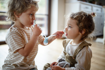 two small children brother and sister at home, playing with nasal aspirator.