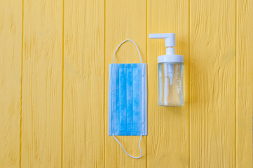 Hand sanitizer bottle and respiratory face mask on yellow wooden background. Stop coronavirus concept. Using antibacterial gel for hands during quarantine