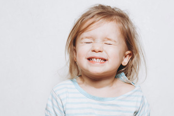 portrait of a little girl of 2 years wearing a red hat and being photographed showing different emotions against a light wall