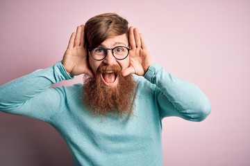 Canvas Print - Handsome Irish redhead man with beard wearing glasses over pink isolated background Smiling cheerful playing peek a boo with hands showing face. Surprised and exited