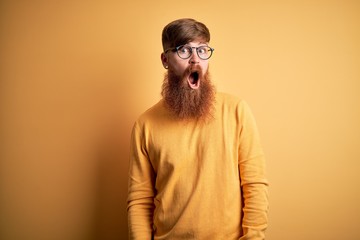 Sticker - Handsome Irish redhead man with beard wearing glasses over yellow isolated background In shock face, looking skeptical and sarcastic, surprised with open mouth