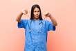 young latin nurse looking sad, disappointed or angry, showing thumbs down in disagreement, feeling frustrated against pink wall