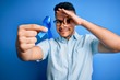 © Krakenimages.com - Young handsome man holding blue cancer ribbon standing over isolated background with happy face smiling doing ok sign with hand on eye looking through fingers