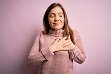 Sticker - Beautiful young woman wearing turtleneck sweater over pink isolated background smiling with hands on chest with closed eyes and grateful gesture on face. Health concept.