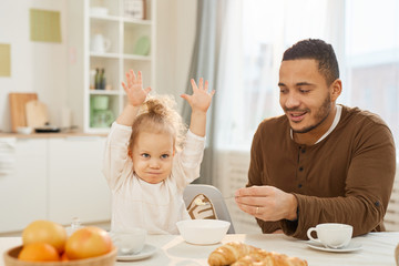 Young man treating his cheerful daughter with tasty breakfast meal in morning at home