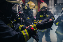 Firemen In Uniform Wearing Gloves And Gas Masks Inside The Fire Department