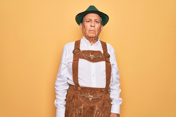 Poster - Senior grey-haired man wearing german traditional octoberfest suit over yellow background Relaxed with serious expression on face. Simple and natural looking at the camera.