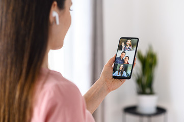 Wall Mural - Video communication via smartphone. A young woman is using phone app for video call, online meeting. She talks with a several people together in same time. Close-up back view