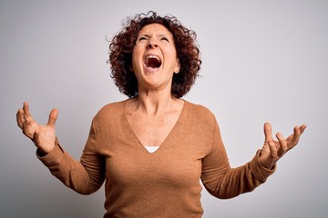 Poster - Middle age beautiful curly hair woman wearing casual sweater over isolated white background crazy and mad shouting and yelling with aggressive expression and arms raised. Frustration concept.