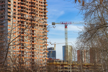 Tower cranes constructing a new residential building. Construction work site and high rise building against blue sky. Construction company or buildings industry concept