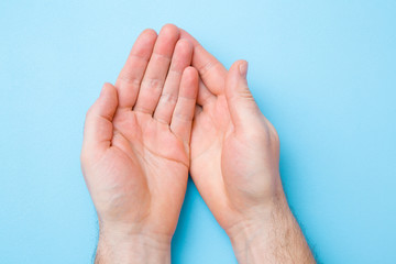 Opened man palms on light blue table background. Pastel color. Closeup. Point of view shot. Top down view.