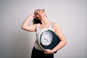 Sticker - Young beautiful woman with curly hair holding weighing machine over white background smiling confident touching hair with hand up gesture, posing attractive and fashionable