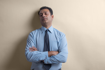 Wall Mural - Businessman with eyes closed standing with his back against a wall with arms crossed
