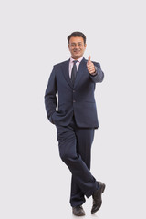 Wall Mural - Portrait of a smiling businessman in eyeglasses showing thumbs up sign with the other hand in pocket
