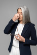 © LIGHTFIELD STUDIOS - tired asian businesswoman with grey hair holding eyeglasses isolated on grey