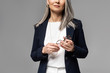 © LIGHTFIELD STUDIOS - cropped view of businesswoman with grey hair holding eyeglasses isolated on grey