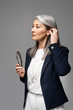 © LIGHTFIELD STUDIOS - asian businesswoman with grey hair holding eyeglasses isolated on grey