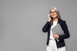 © LIGHTFIELD STUDIOS - corporate asian businesswoman with grey hair talking on smartphone and holding laptop isolated on grey