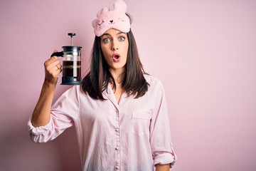 Young brunette woman with blue eyes wearing pajama making coffee with french coffeemaker scared in shock with a surprise face, afraid and excited with fear expression