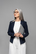 © LIGHTFIELD STUDIOS - confident asian businesswoman with grey hair holding laptop isolated on grey