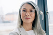 © LIGHTFIELD STUDIOS - attractive confident asian businesswoman with grey hair in grey suit and eyeglasses looking at camera