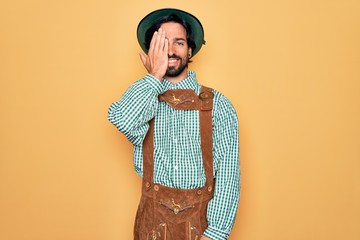 Wall Mural - Young handsome man wearing tratidional german octoberfest custome for Germany festival covering one eye with hand, confident smile on face and surprise emotion.