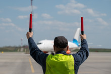 Male Airport Marshal With Electric Wands In A Yellow Uniform Helps Park The Plane. The Supervisor Meets A Passenger Plane At The Airport. The Plane Steers Into The Parking Lot.