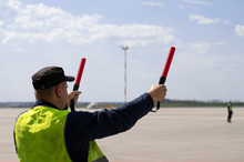 An Airport Marshal In A Yellow Uniform Helps Signals To Park By Plane. The Supervisor Meets A Passenger Plane At The Airport. The Plane Steers Into The Parking Lot.