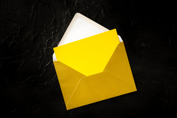 Wall Mural - A yellow greeting card in a golden envelope mock-up, shot from the top on a black background with a place for text