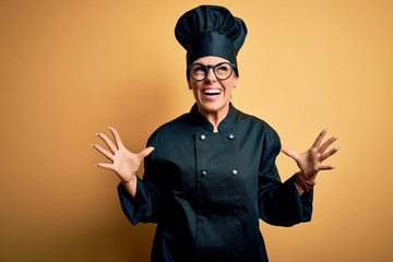 Sticker - Young beautiful brunette chef woman wearing cooker uniform and hat over yellow background crazy and mad shouting and yelling with aggressive expression and arms raised. Frustration concept.