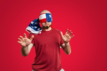 The man with the American flag tied around his eyes held his hands out like a blind man. Red background. The concept of freedom, patriotism and protest