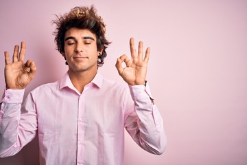 Young handsome man wearing king crown standing over isolated pink background relax and smiling with eyes closed doing meditation gesture with fingers. Yoga concept.