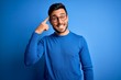 © Krakenimages.com - Young handsome man with beard wearing casual sweater and glasses over blue background Smiling pointing to head with one finger, great idea or thought, good memory