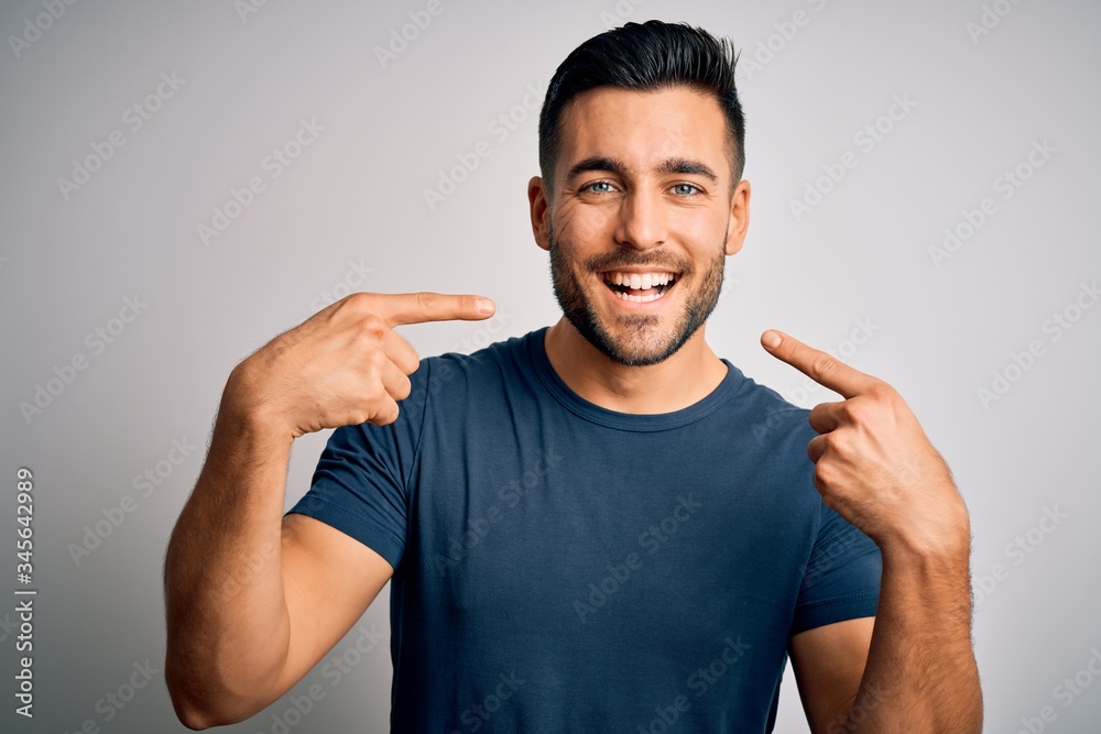 Young handsome man wearing casual t-shirt standing over isolated white background smiling cheerful showing and pointing with fingers teeth and mouth. Dental health concept.