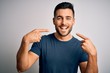 Leinwandbild Motiv Young handsome man wearing casual t-shirt standing over isolated white background smiling cheerful showing and pointing with fingers teeth and mouth. Dental health concept.
