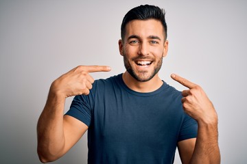 Wall Mural - Young handsome man wearing casual t-shirt standing over isolated white background smiling cheerful showing and pointing with fingers teeth and mouth. Dental health concept.
