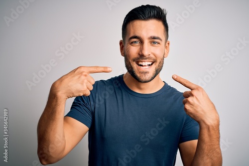 Fotografía Young handsome man wearing casual t-shirt standing over isolated white background smiling cheerful showing and pointing with fingers teeth and mouth
