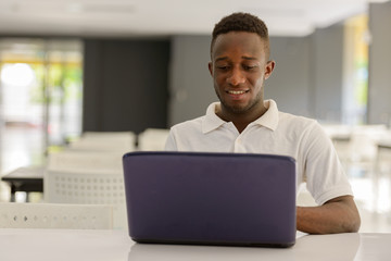 Wall Mural - Portrait of happy young African man using laptop inside modern building