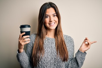 Sticker - Young beautiful girl drinking cup of coffee standing over isolated white background very happy pointing with hand and finger to the side