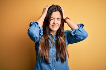 Poster - Young beautiful girl wearing casual denim shirt standing over isolated yellow background suffering from headache desperate and stressed because pain and migraine. Hands on head.