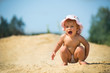 Front view of adorable child screaming and squatting on sand. Toddler wearing white summer hat. Concept of childhood and summer.
