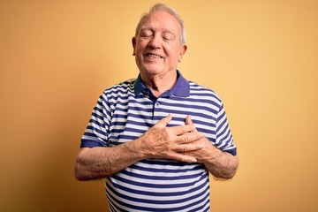 Sticker - Grey haired senior man wearing casual navy striped t-shirt standing over yellow background smiling with hands on chest with closed eyes and grateful gesture on face. Health concept.